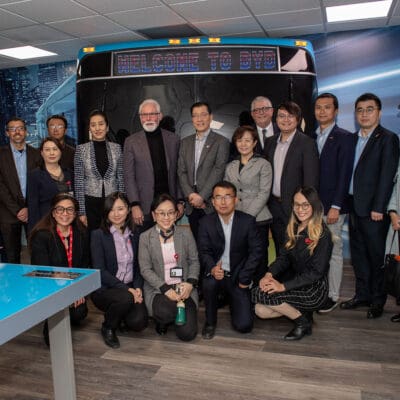 A group of people in business attire stands together, posing for a photo in front of a sign that reads "Welcome to BYD.