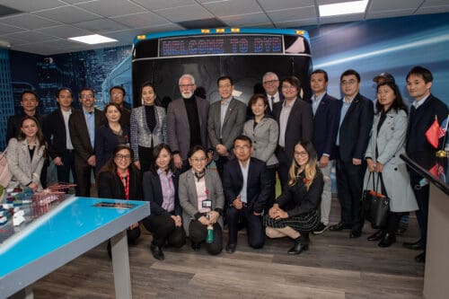 A group of people in business attire stands together, posing for a photo in front of a sign that reads "Welcome to BYD.