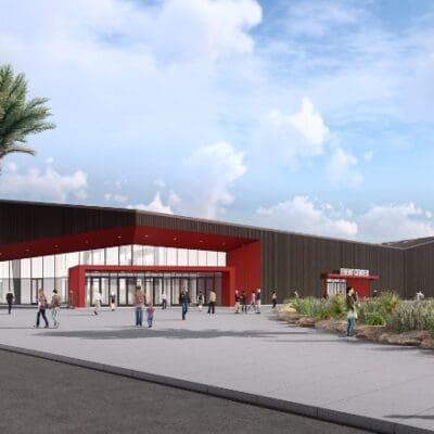 Modern event center with red and black exterior, large windows, and an entrance sign that reads "EVENT CENTER." Palm trees line the sidewalk, and people are walking around the area.