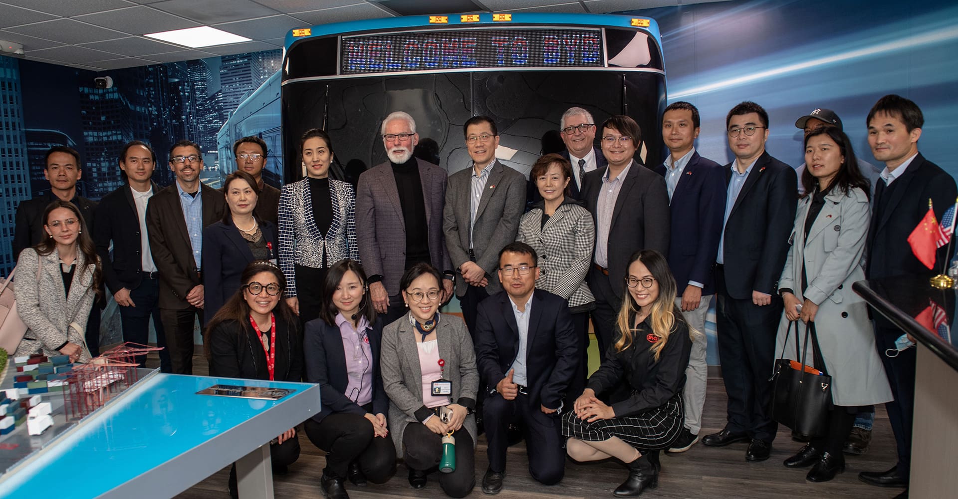 A group of people, dressed in business attire, posing for a photo in front of a display that reads "Welcome to BYD" in a modern, well-lit room.