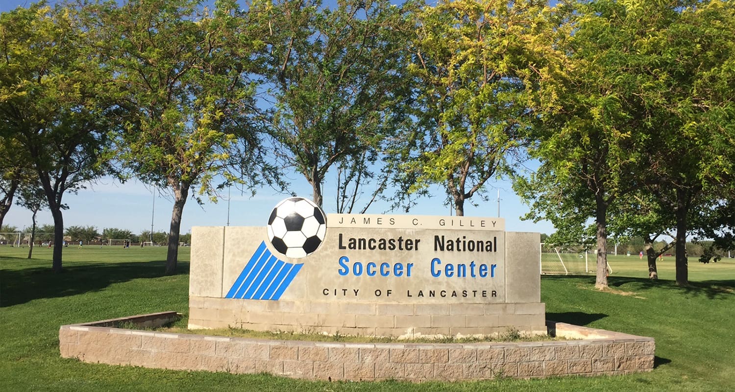 Sign for the Lancaster National Soccer Center in Lancaster, surrounded by greenery and trees, featuring a soccer ball graphic and the name "James C. Gilley.