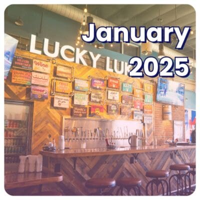 A bar with wooden stools, beverage taps, and a colorful array of drink signs proudly showcases the Lucky Luke signage above. Celebrated as the business of the month, this lively spot buzzes with excitement as January 2025 gleams in the foreground.