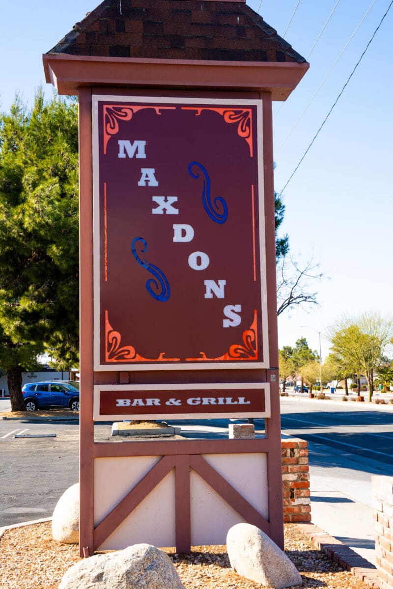 Sign for Maxdons Bar & Grill with decorative elements, surrounded by trees and a clear sky background.