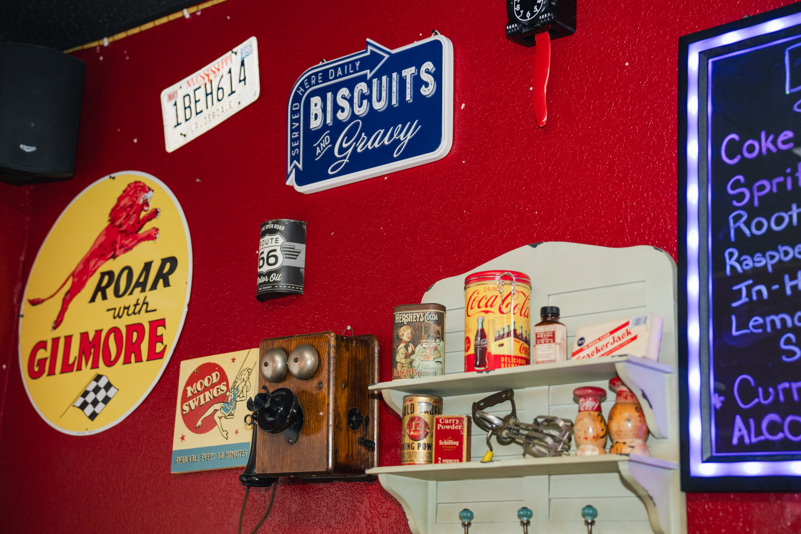 Vintage signs, food tins, and an antique wall telephone displayed against a bright red wall inside Cracker Jack’s BBQ.