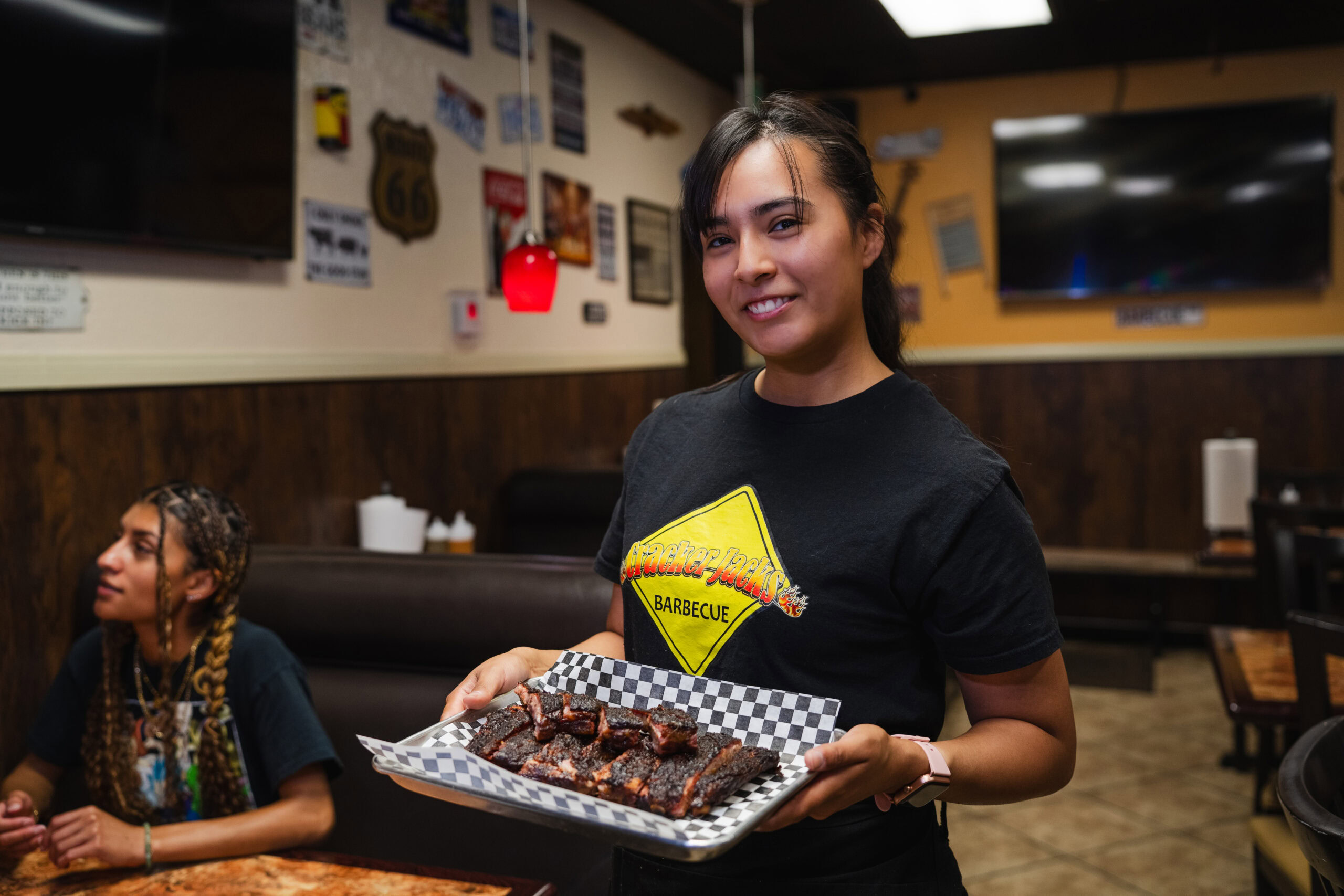 Smiling Cracker Jack’s BBQ server holding a tray of sliced, sauce-glazed ribs in the dining room.