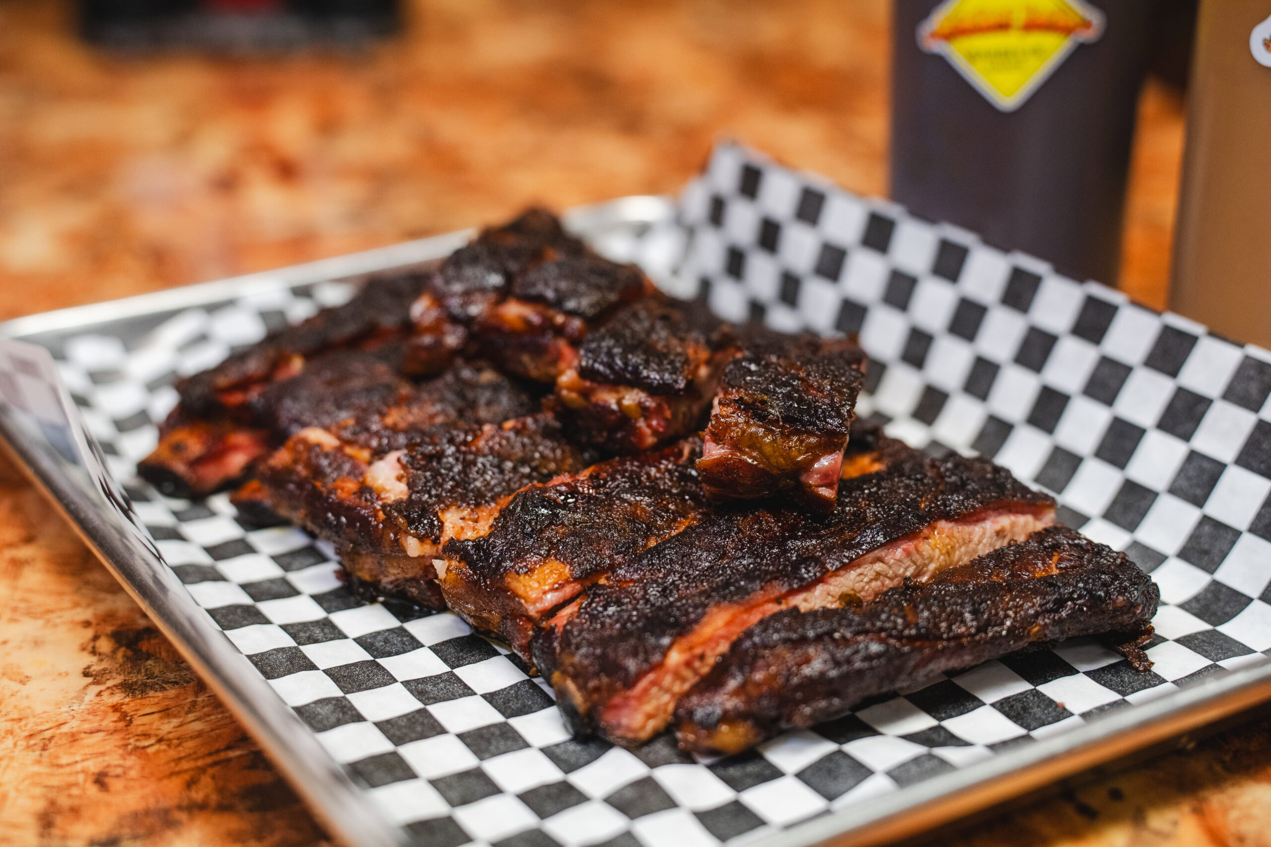 Sliced smoked ribs with a dark, seasoned crust served on checkered paper at Cracker Jack’s BBQ.