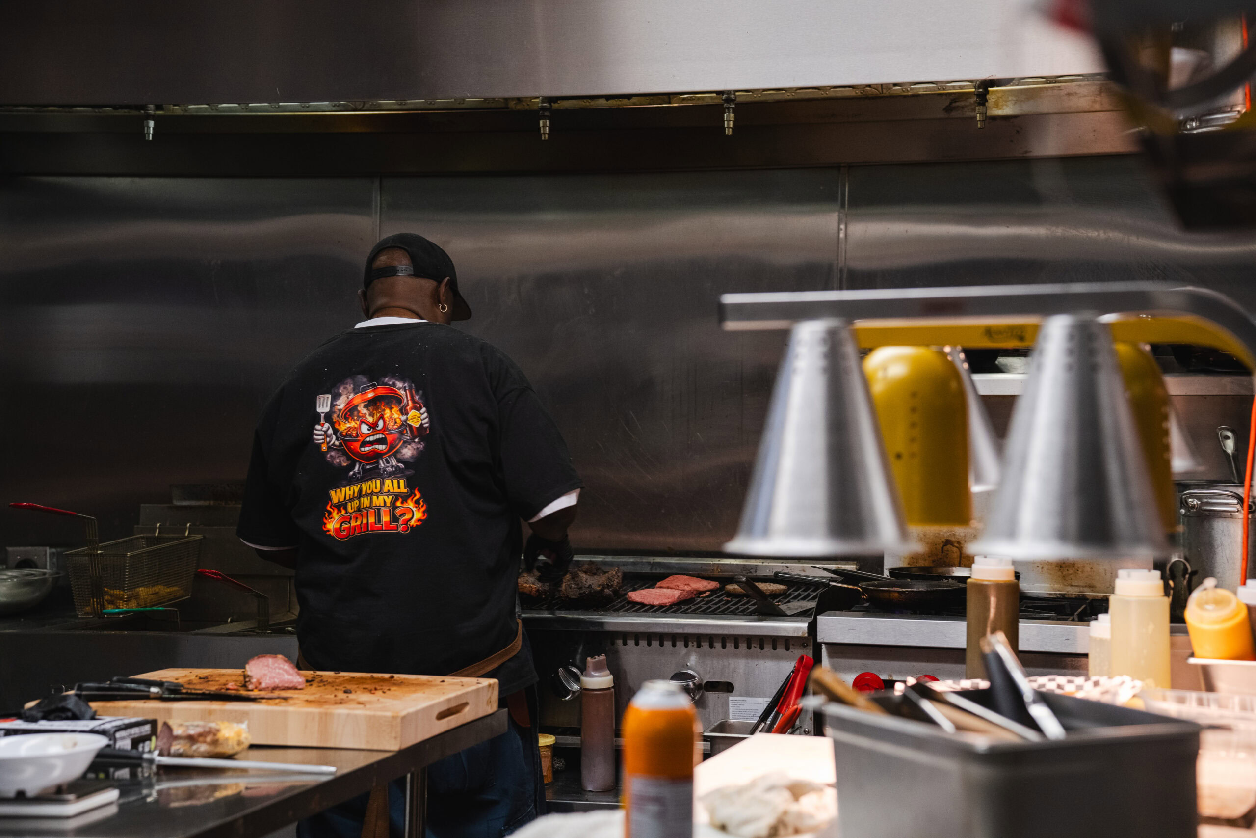 A cook tends meat on the grill in Cracker Jack’s BBQ’s stainless-steel kitchen.