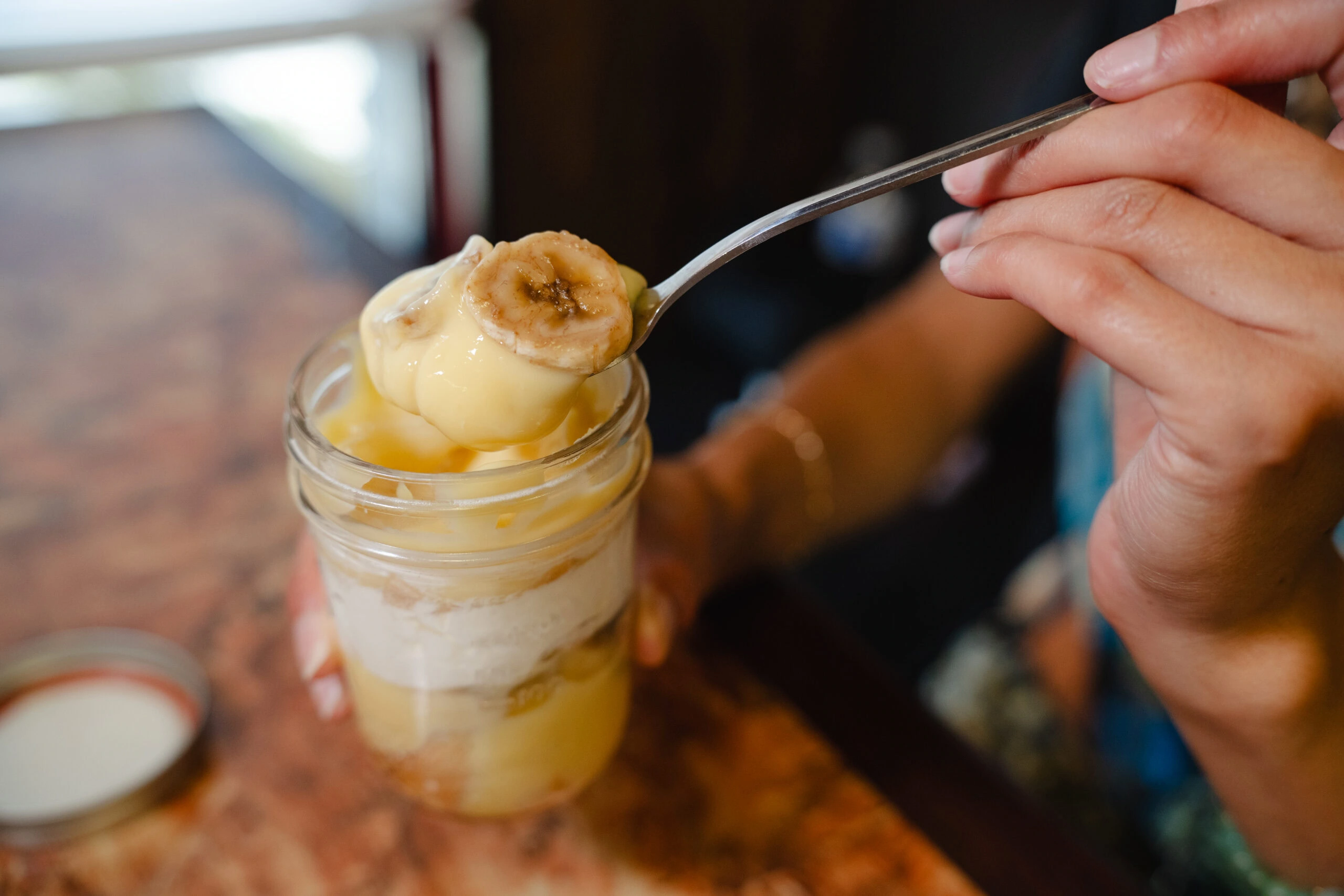 A spoonful of banana pudding lifted from a layered dessert served in a mason jar.