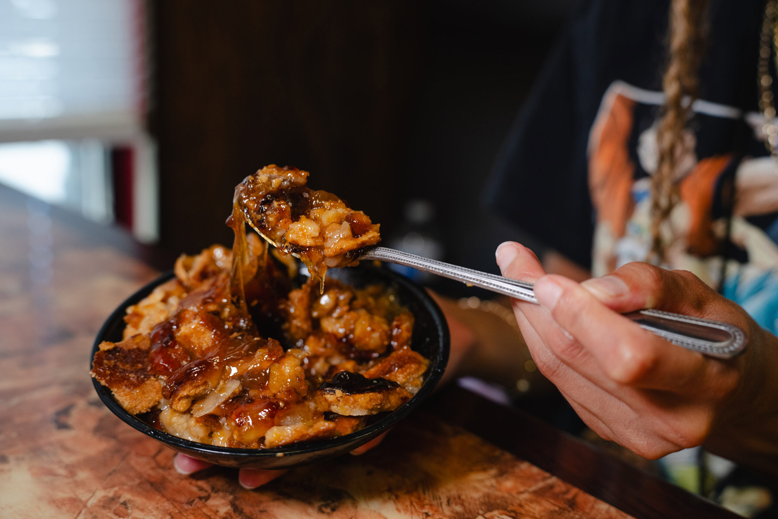 A spoonful of warm peach cobbler lifted from a bowl of fruit, crust, and syrup.